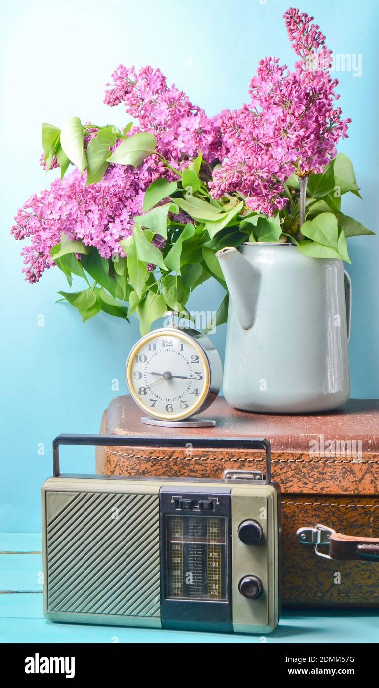 Bouquet de lilas dans une bouilloire émaillée sur une valise ancienne, radio  vintage, réveil sur fond bleu. Style rétro encore plus vivant Photo Stock -  Alamy