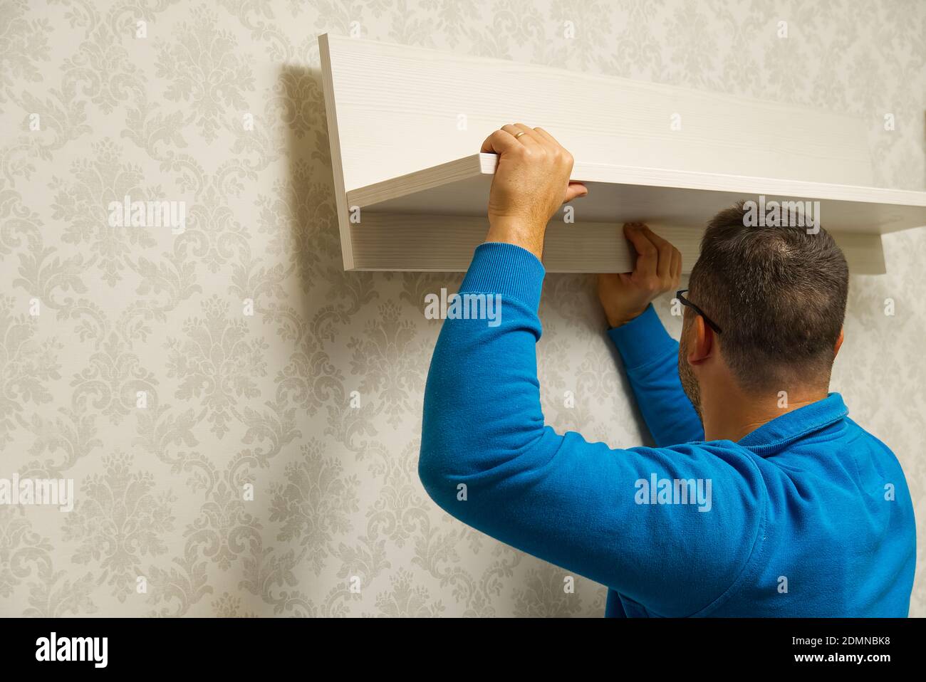 le maître de maison est fixé à l'étagère sur un mur en béton avec des fonds d'écran. le maître assemble des meubles. Banque D'Images