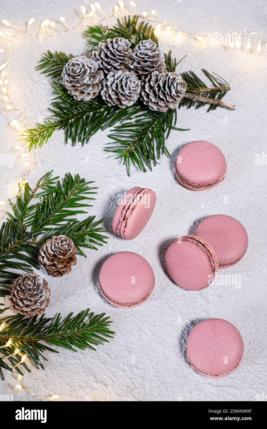 Macarons de figue magnifiquement arrangés sur une table blanche, l'hiver décoré avec des branches de sapin et des cônes de pin, une chaîne de Lichter brille en arrière-plan Banque D'Images