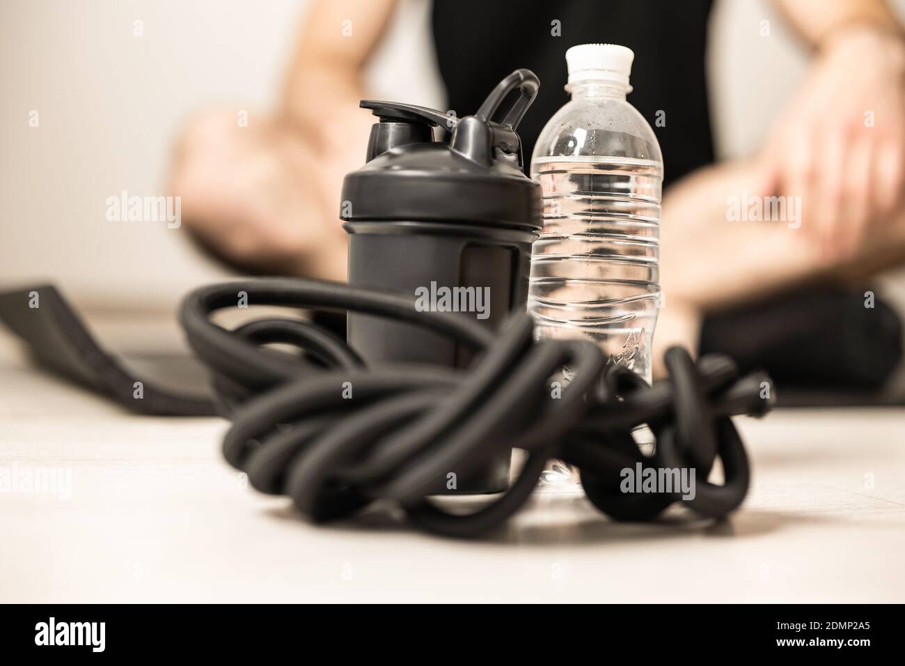 Gros plan sur l'équipement sportif. Bouteille de sport, bouteille d'eau en plastique, bande de résistance. Homme flou dans le siège facile poser assis avec les jambes croisant. Entraînement à Banque D'Images