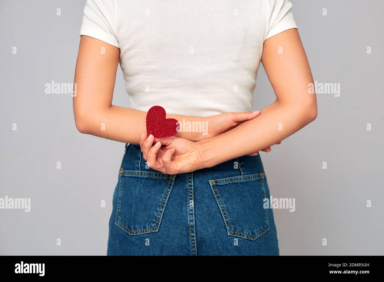 amour secret. jeune femme tenant un petit coeur rouge étincelant derrière son dos. partager ou recevoir de la valentin, garder l'amour sur vous. Banque D'Images