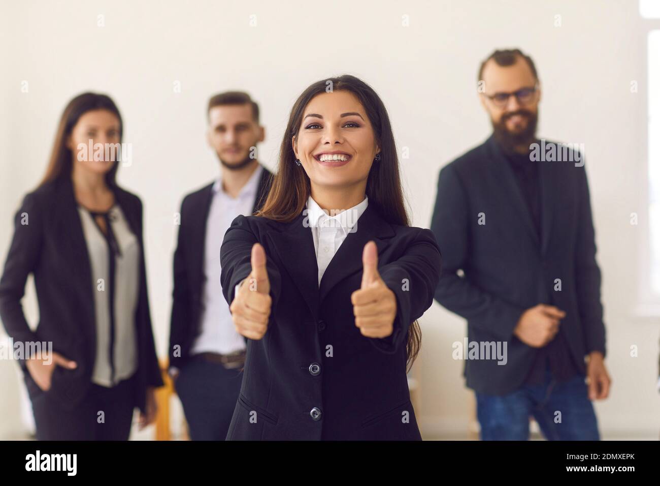 Femme d'affaires souriante ou chef de groupe qui donne le pouce à l'équipe de travailleurs en arrière-plan Banque D'Images