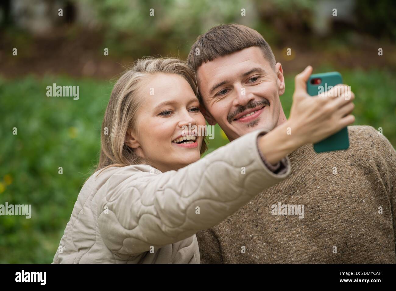 Un jeune mari et une femme prennent un selfie ensemble sur un smartphone pour un blog sur un réseau social sur un fond vert. Gros plan Banque D'Images