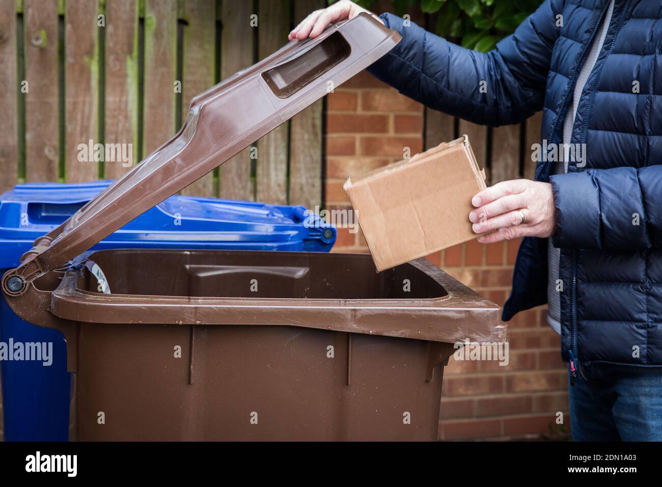 Un responsable plaçant une boîte en carton marron dans un bac de recyclage sur le trottoir prêt pour la collecte et le recyclage par le Au Royaume-Uni Banque D'Images