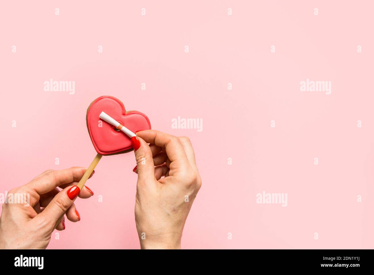 La femme dévoile une note d'amour sur un cookie en forme de cœur sur fond rose. Carte de vœux avec espace de copie. Banque D'Images