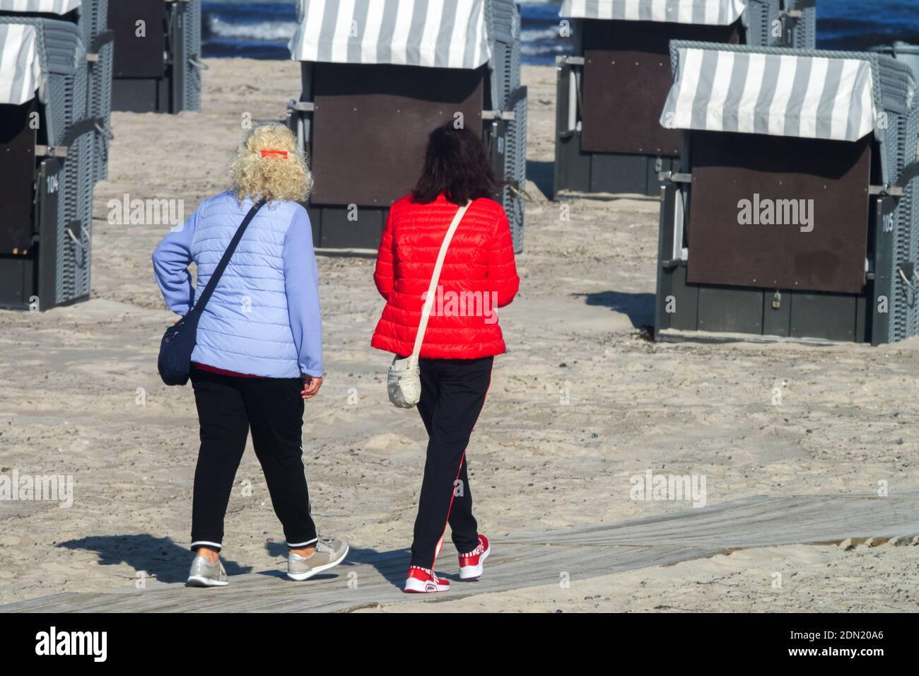 Une paire de femmes marchant loin de la plage parmi des chaises de plage en osier dans le soleil de la fin de l'été, Allemagne Warnemunde Banque D'Images