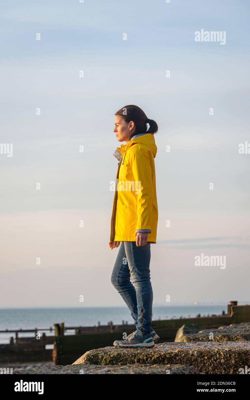 Femme adulte portant une veste jaune, avec vue sur la mer. Concept seul. Banque D'Images