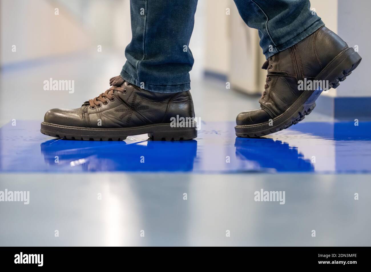 Homme dans les chaussures brunes marcher sur les tapis adhésifs bleus. Banque D'Images