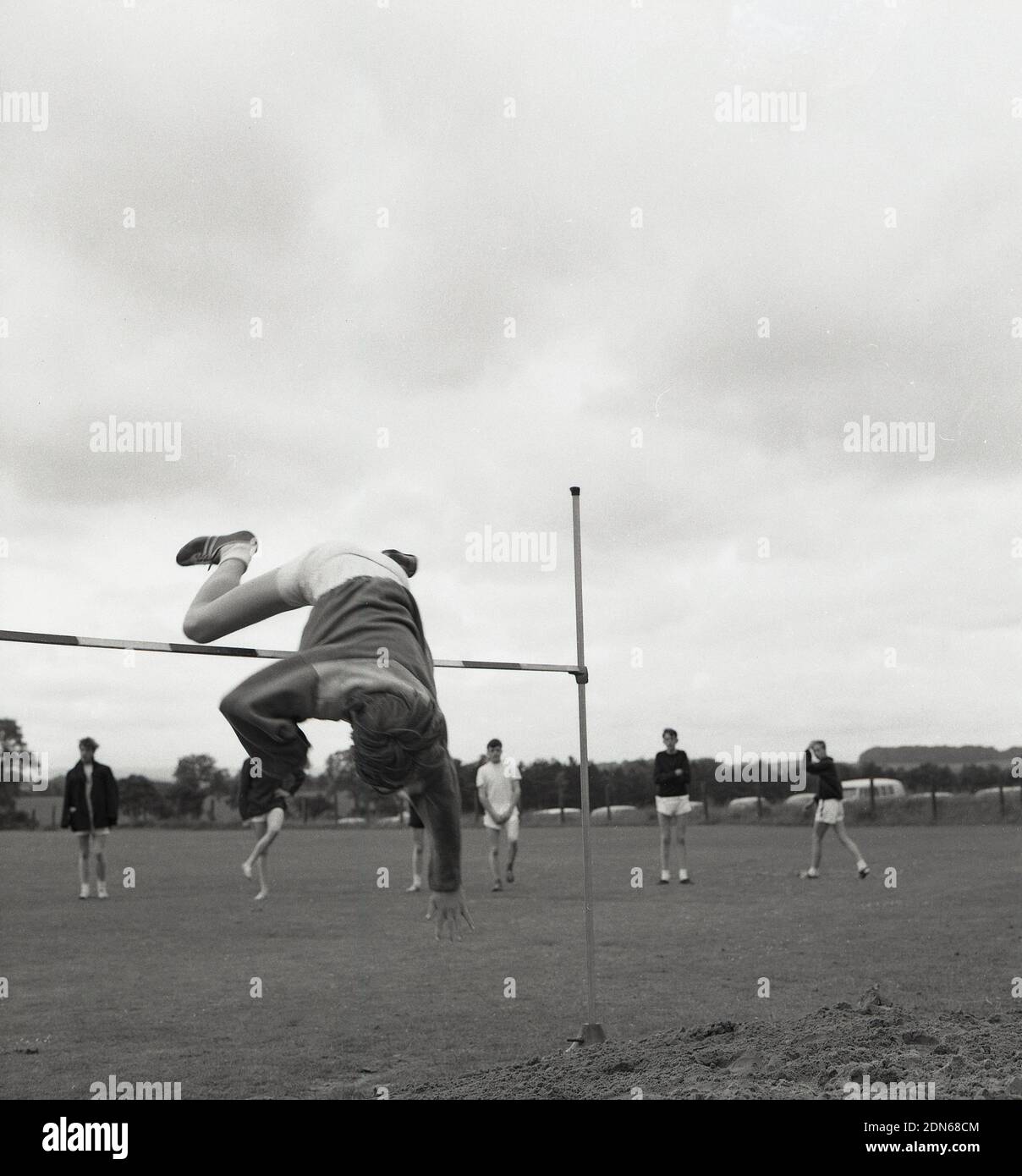 1960s, historique, un adolescent effectuant le saut à la hauteur lors d'une journée de sport à l'école secondaire, en plein air en utilisant la version de plongée de la méthode de saut à la vitesse, avec sa tête et les bras passant par le bar en premier, suivi de son tronc et des jambes, Fife, Écosse, Royaume-Uni. La technique de la selle était le style principal dans le saut en hauteur avant le développement de la Fosbury Flop. Médaillé d'or aux Jeux Olympiques de 1964, Valeriy Brumel a utilisé la variante de plongée de la selle. Banque D'Images