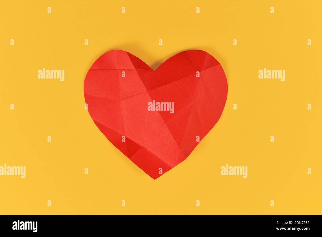 Coeur en papier rouge avec lignes pliantes sur fond jaune. Concept pour coeur brisé ou malade Banque D'Images
