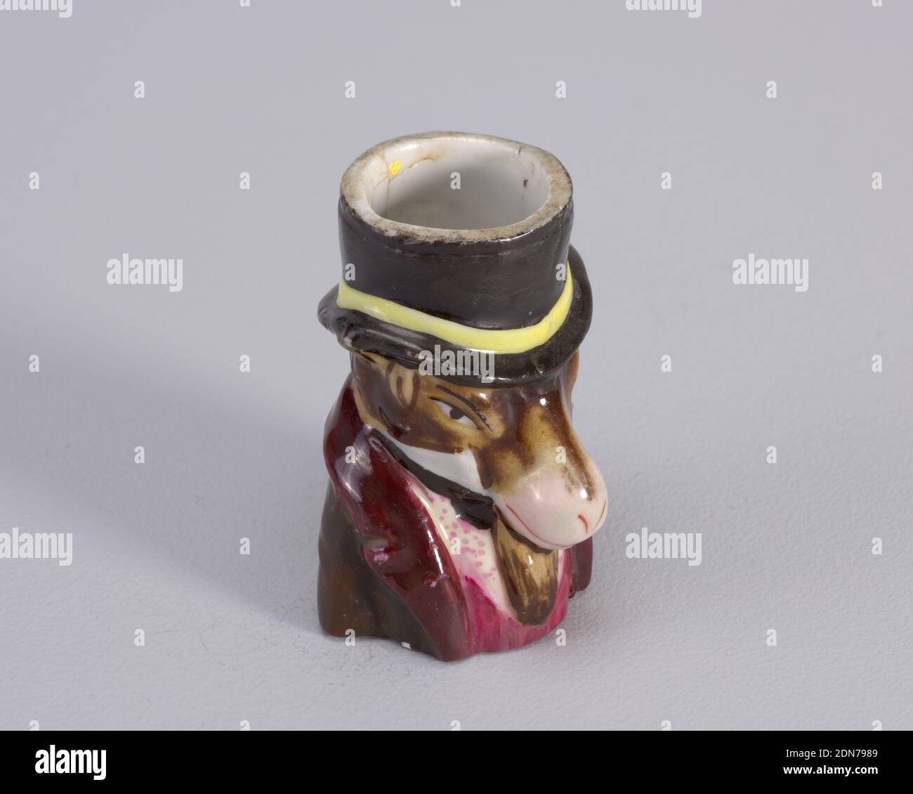 Matchsafe, porcelaine, figurine d'âne portant un chapeau haut avec bande  jaune. Figure porte également un manteau de boron avec un gilet magenta et  une chemise blanche avec des points magenta., probablement Angleterre,