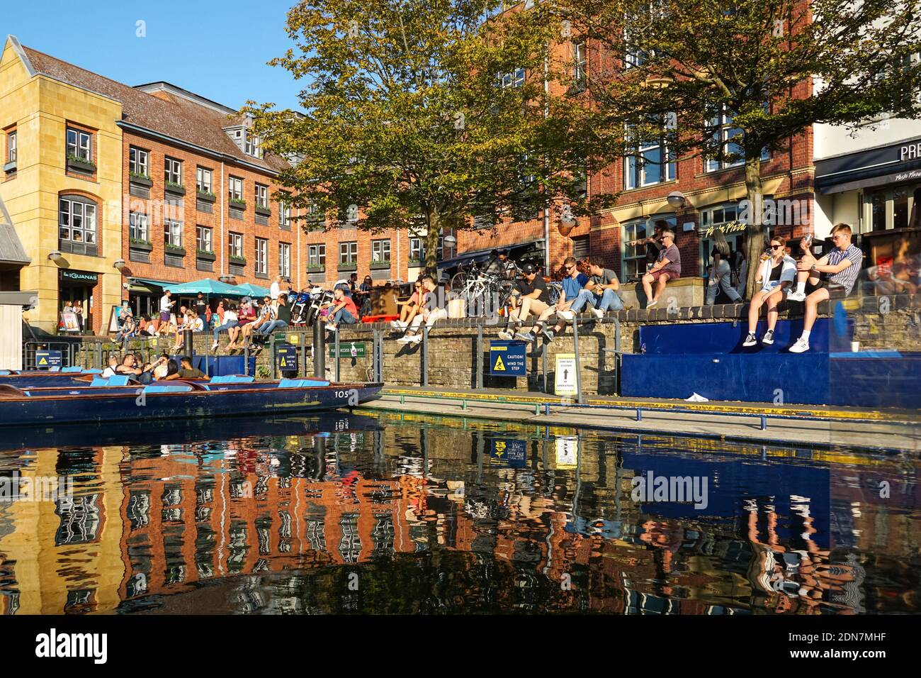 Jeunes assis et buvant sur la rive de la rivière Cam à Cambridge, Cambridgeshire Angleterre Royaume-Uni Banque D'Images