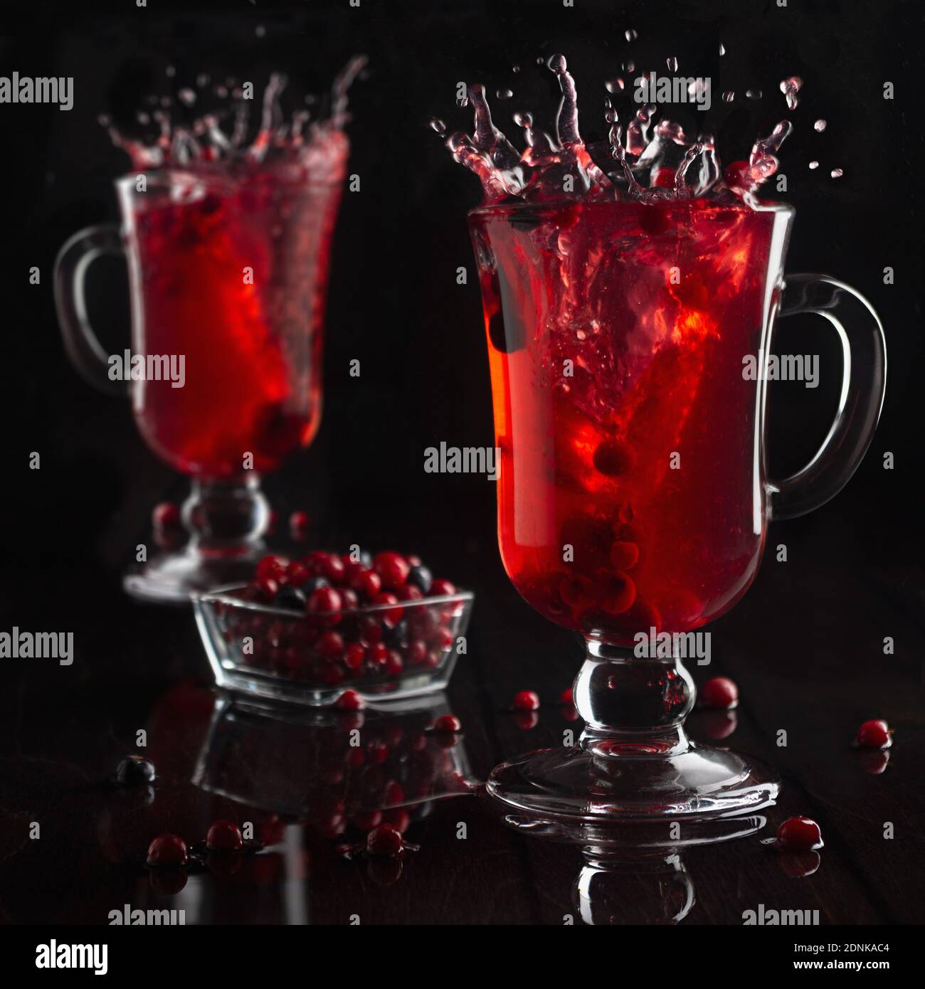 Vin chaud rouge vif avec baies et deux verres à vin en verre dans un intérieur noir foncé, carré. Banque D'Images