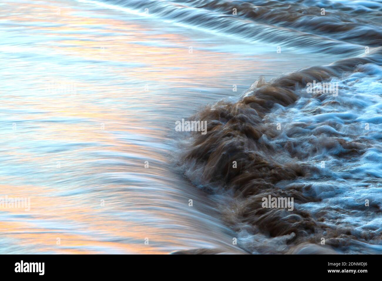 La marée se déverse sur les échalotes d'une plage au crépuscule, reflétant les couleurs du coucher de soleil dans l'eau en mouvement rapide. Banque D'Images