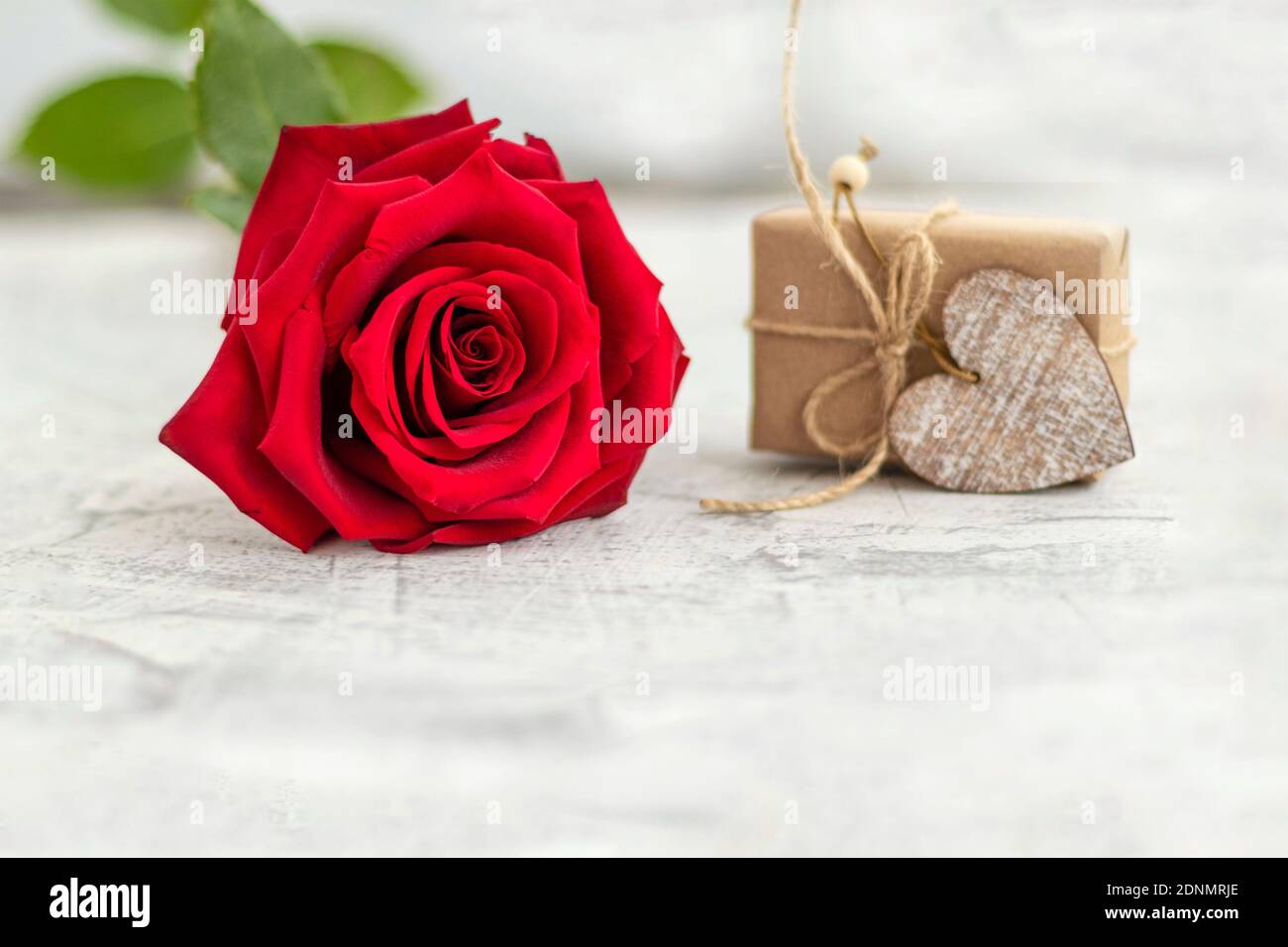 Cadeau emballé dans du papier artisanal à côté de la rose rouge sur fond de pierre blanche. Cadeau romantique pour la Saint-Valentin avec espace pour le texte. Concept de proposition de mariage. Mise au point douce. Copier l'espace Banque D'Images