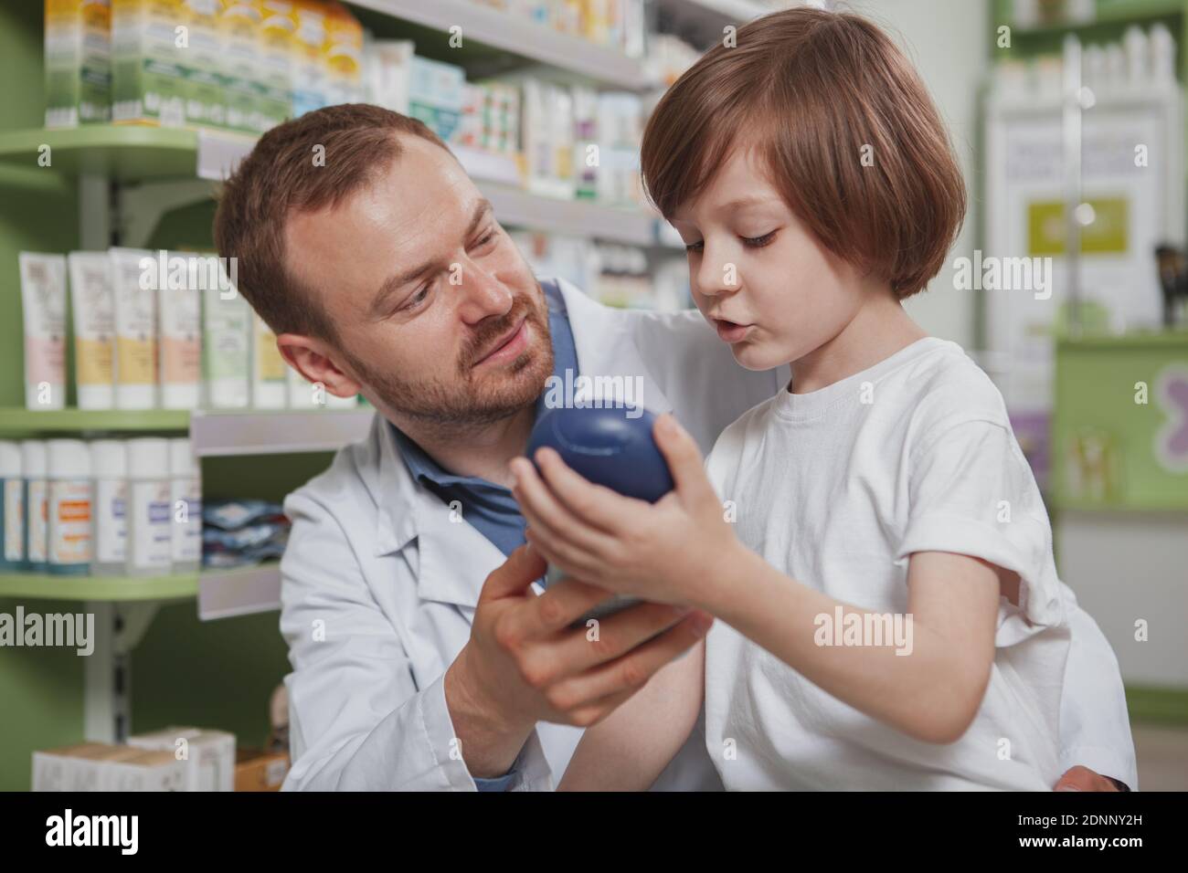 Gros plan d'un pharmacien masculin mature aidant le petit garçon à choisir du shampooing à acheter. Mignon petit garçon parlant au chimiste, shopping à la pharmacie Banque D'Images