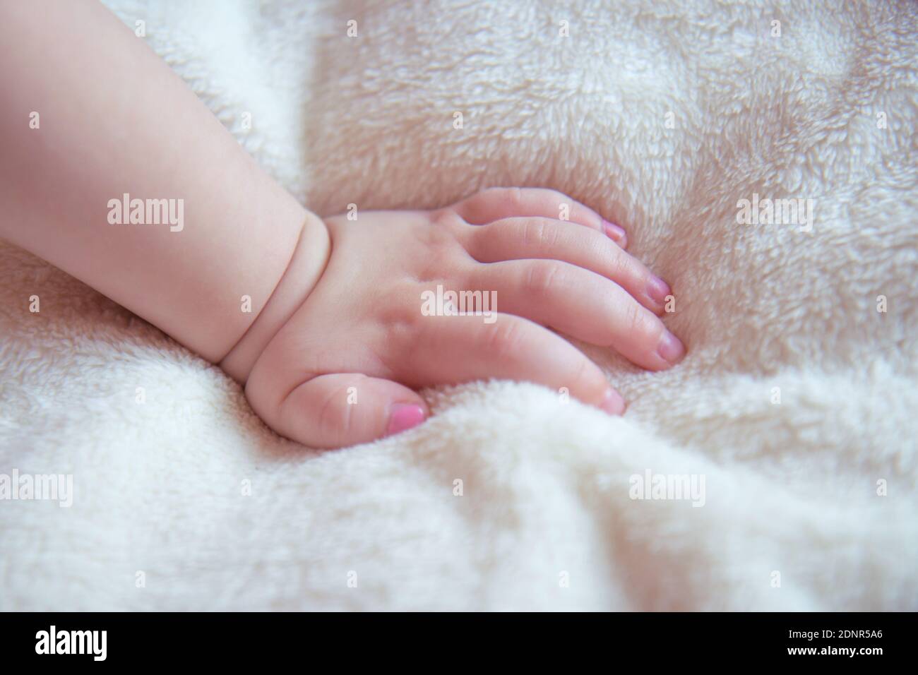 Main de bébé sur une couverture douce et moelleuse beige. Ongles sur la main d'une petite fille peint avec vernis à ongles rose Banque D'Images