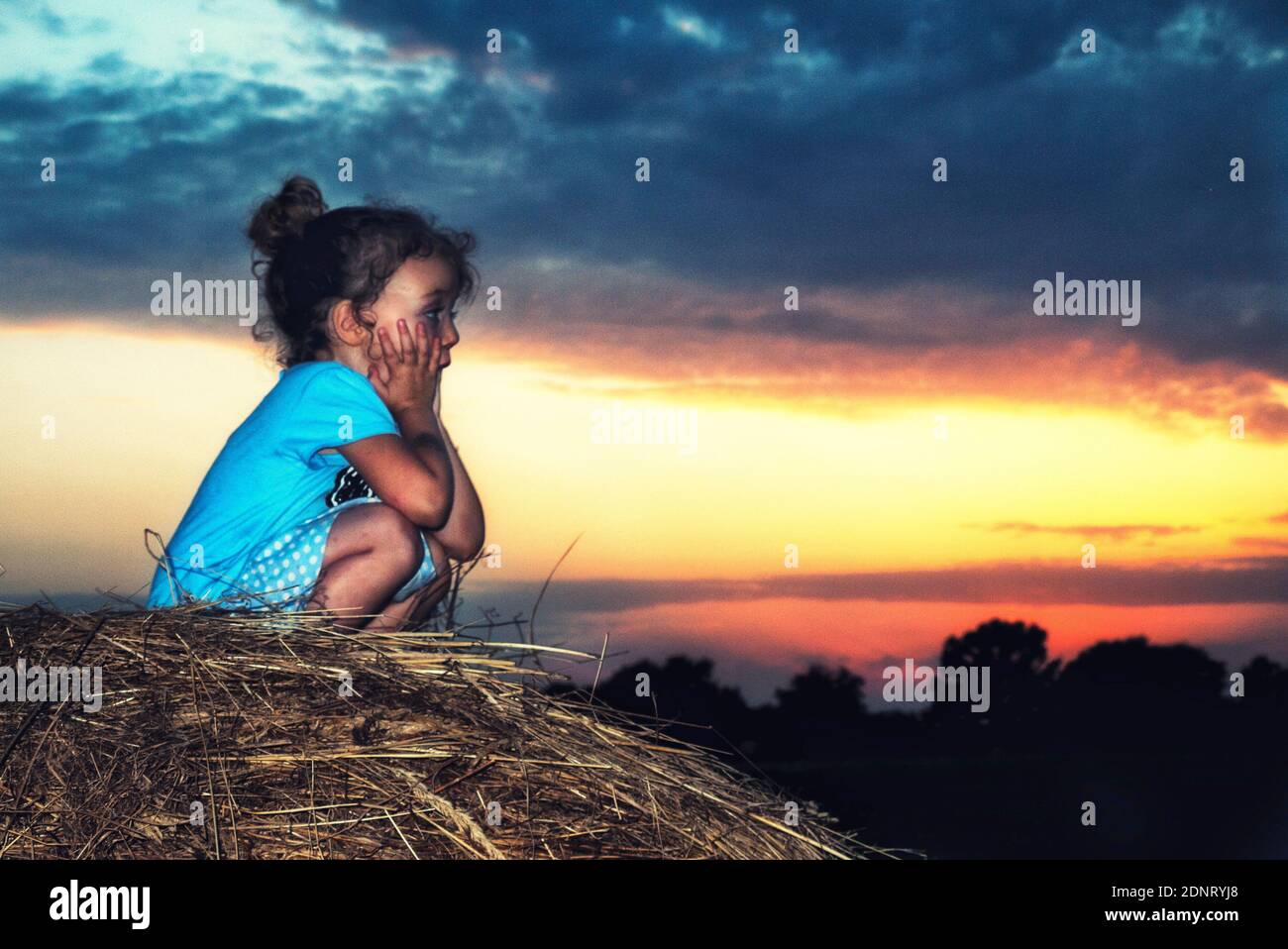 Portrait d'une fille assise sur une balle de foin au coucher du soleil, Pologne Banque D'Images