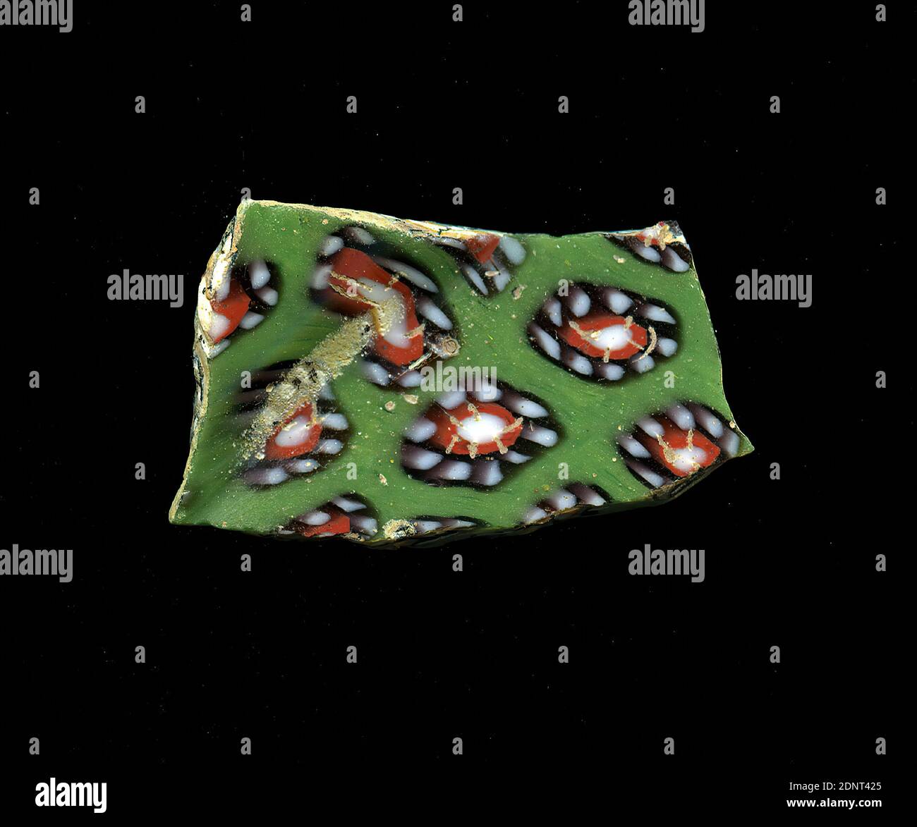 Fragment d'un vaisseau, verre, technique millefiori, Total: Hauteur: 2.20 cm; largeur: 3.80 cm, conteneur, stockage, cuisine, boisson et barque, ornements floraux, début de la période impériale, UNE légère courbure du fragment de verre permet l'attribution à un vaisseau, éventuellement un bol. Le shard vert montre plusieurs fleurs dans la technique de millefiori. Autour d'un point blanc avec un contour rouge se trouve une bande violette avec des points blancs comme pétales. Pour la production, des verres de différentes couleurs ont été formés sur des tubes et des tiges. Ils ont été pressés ensemble et chauffés, ce qui a donné une longue tige. Banque D'Images