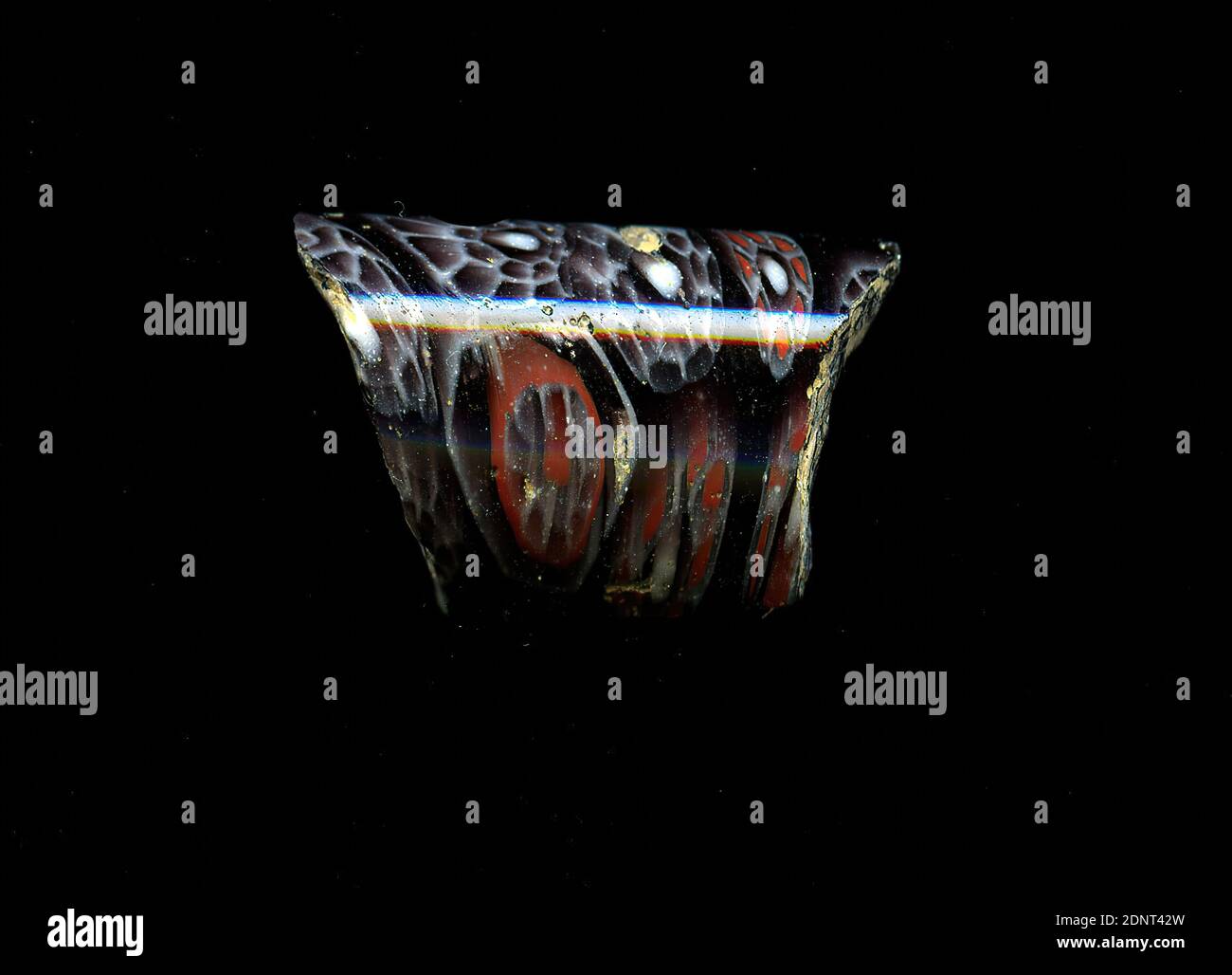 Fragment d'un vaisseau, verre, technique millefiori, Total: Hauteur: 2.20 cm; largeur: 1.40 cm, contenant, stockage, cuisine, ustensiles de boisson et de service, ornements floraux, période impériale précoce, période impériale moyenne, période impériale tardive, UNE légère courbure du fragment de verre permet l'affectation à un vaisseau, éventuellement à un bol. Trois types de fleurs dans la technique de millefiori peuvent être reconnus dans le verre violet: On est situé dans un nid d'abeille blanc, suivi d'un anneau rouge. On y voit la fleur avec son coeur rouge et ses pétales avec des bordures blanches. Banque D'Images