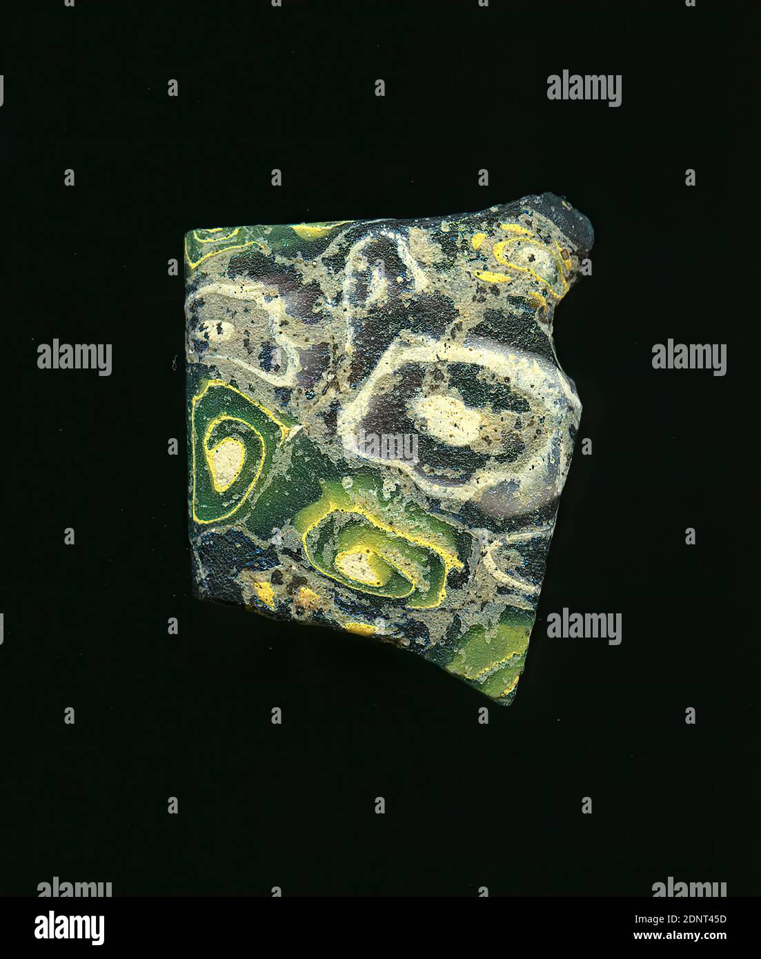 Fragment d'un vaisseau, verre, technique millefiori, Total: Hauteur: 2.20 cm; largeur: 2.80 cm; profondeur: 0.20 cm, conteneur, stockage, travail de cuisine, ornements de fleurs, début de la période impériale, UNE légère courbure du fragment de verre permet l'affectation à un vaisseau. La casade a des parties vertes et pourpres foncé sur lesquelles des spirales jaunes et blanches de différentes tailles peuvent être vues. Pour la production, des verres de différentes couleurs ont été formés en tubes et en tiges. Ils ont été pressés ensemble et chauffés, ce qui a donné une longue tige. Le verre maintenant coupé en tranches avait des motifs amorphes ou floraux différents. Banque D'Images