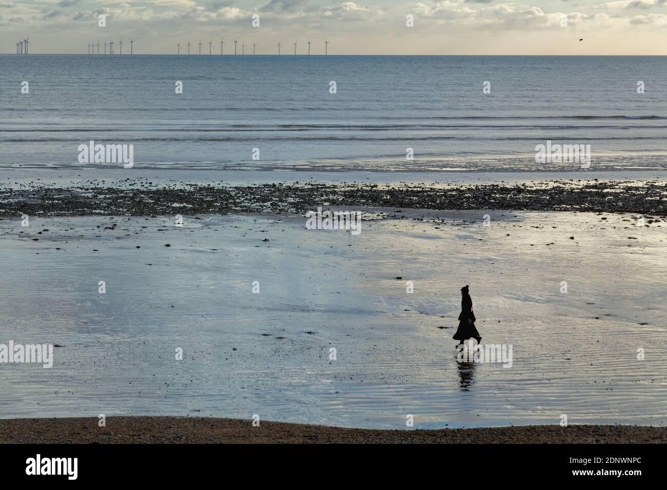 Femme seule en silhouette marchant sur la plage de Worthing avec parc d'éoliennes à l'horizon, Worthing West Sussex Angleterre Banque D'Images