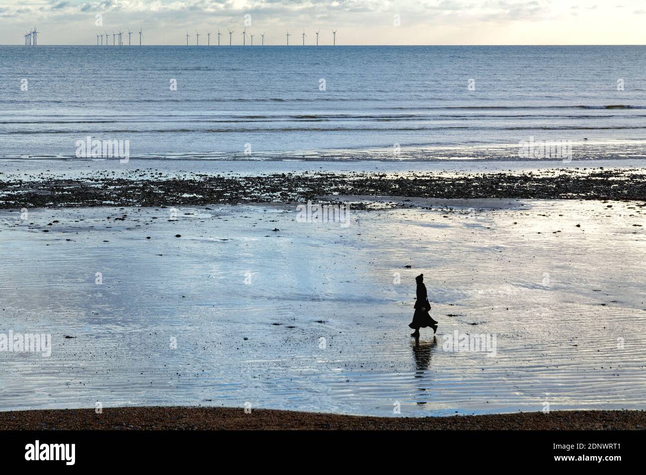Femme seule en silhouette marchant sur la plage de Worthing avec parc d'éoliennes à l'horizon, Worthing West Sussex Angleterre Banque D'Images