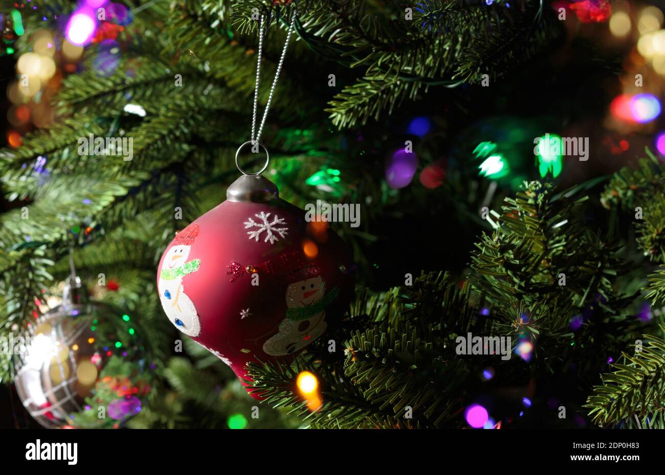 gros plan d'un arbre de noël rouge avec un bonhomme de neige suspendu d'un arbre de noël avec des lumières de bokeh étincelantes autour Banque D'Images