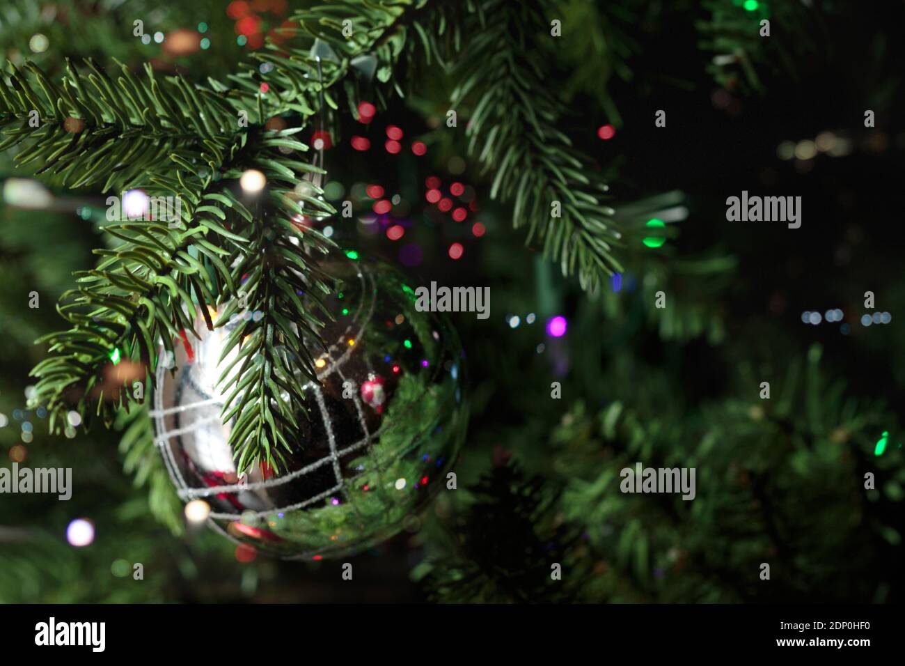 décoration de noël argentée chatoyante suspendue à un sapin de noël entouré de lumières bokeh multicolores Banque D'Images