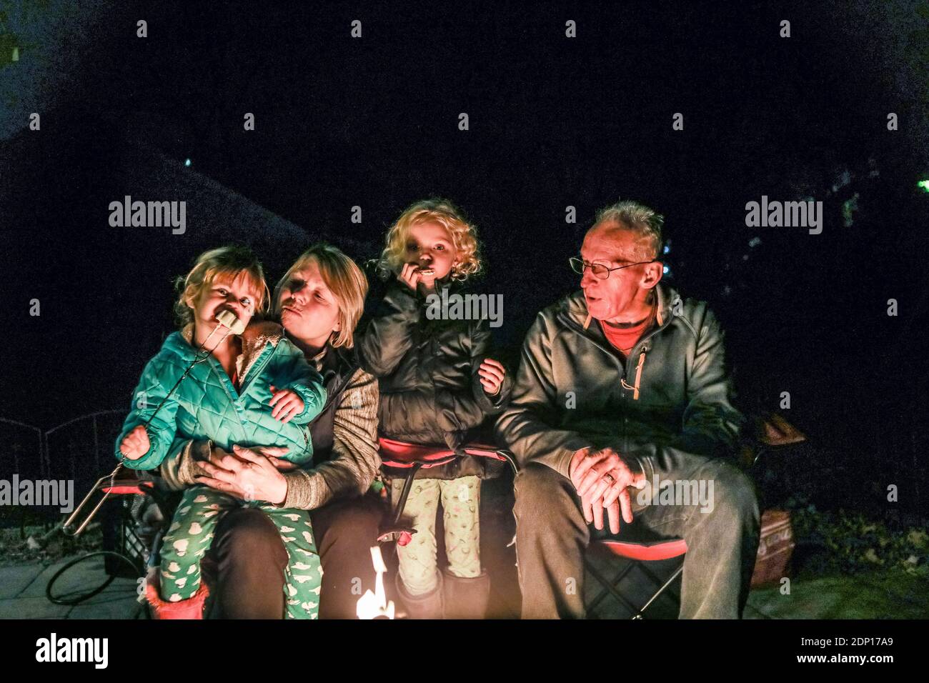 Grands-parents assis avec des petits-enfants autour d'un foyer Banque D'Images