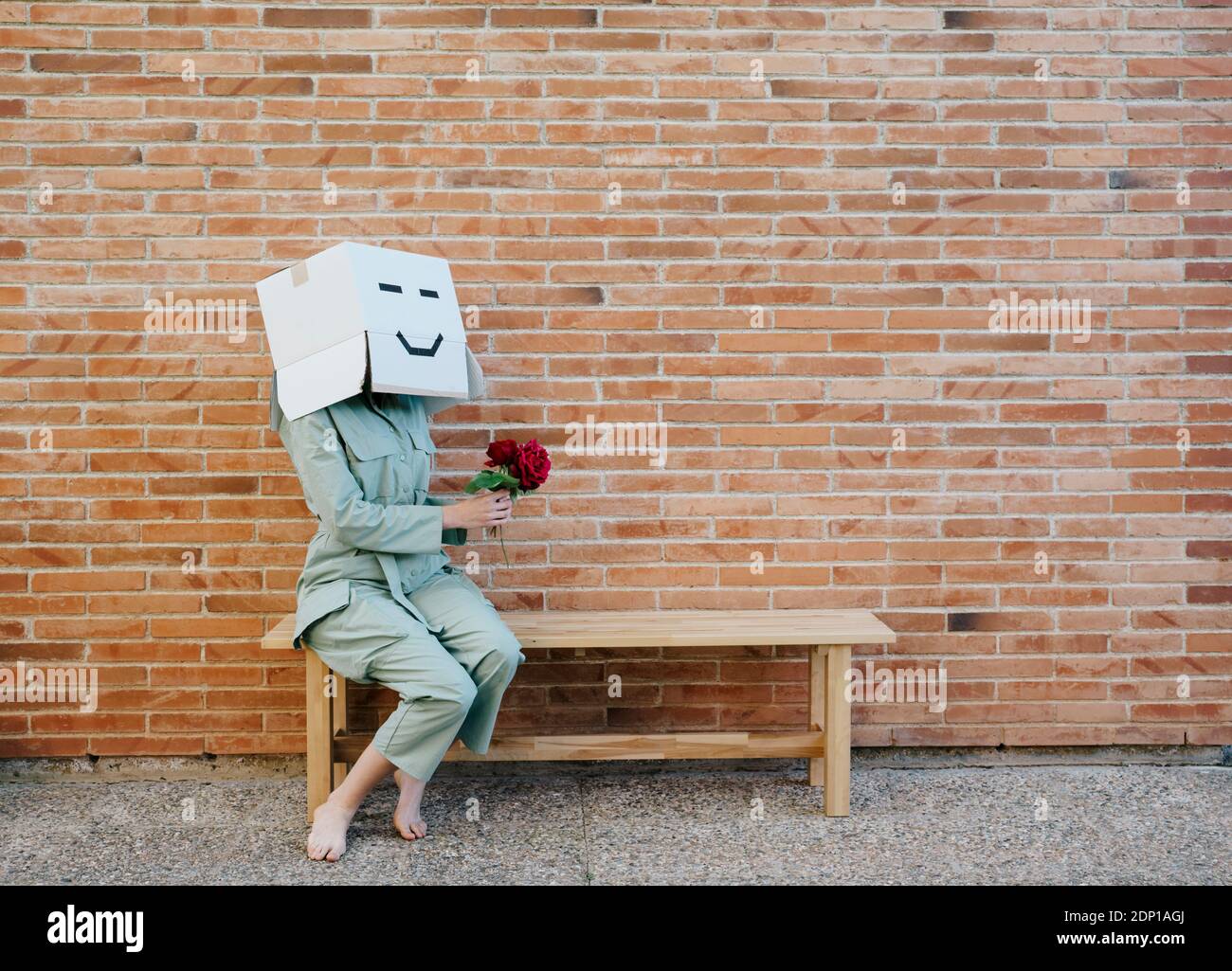 Femme portant une boîte en carton au visage heureux, tenant une rose rouge, assise sur un banc Banque D'Images