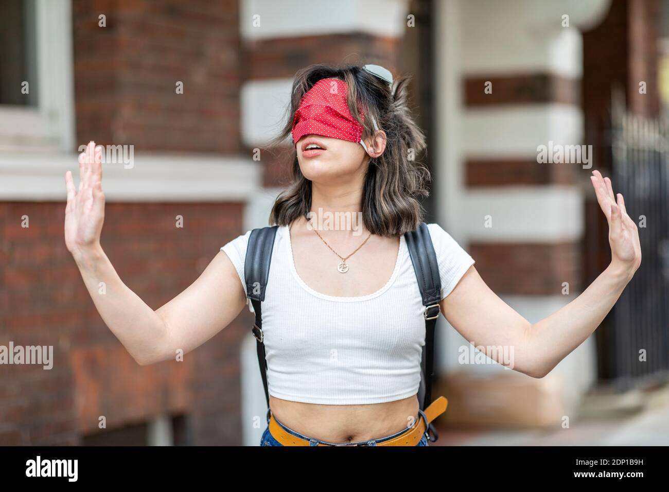 Jeune femme portant un masque rouge sur les yeux gestuelle pendant en ville Banque D'Images