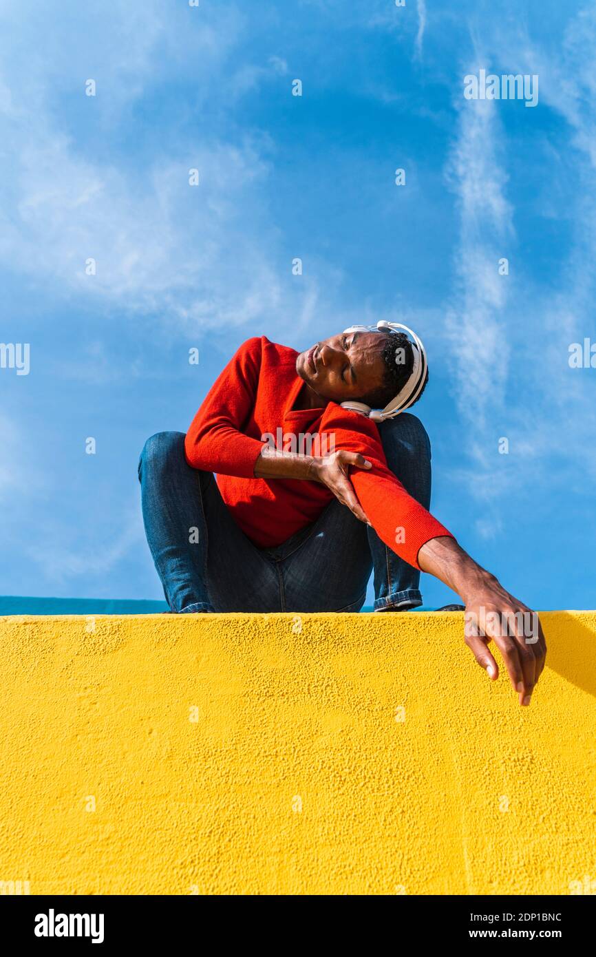 Jeune homme avec des écouteurs, l'écoute de la musique, de la danse sur le mur jaune Banque D'Images