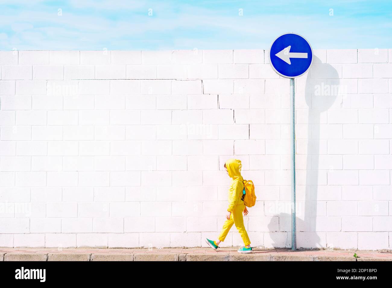 Fille marchant à un panneau de signalisation, direction à gauche en face d'un mur blanc Banque D'Images
