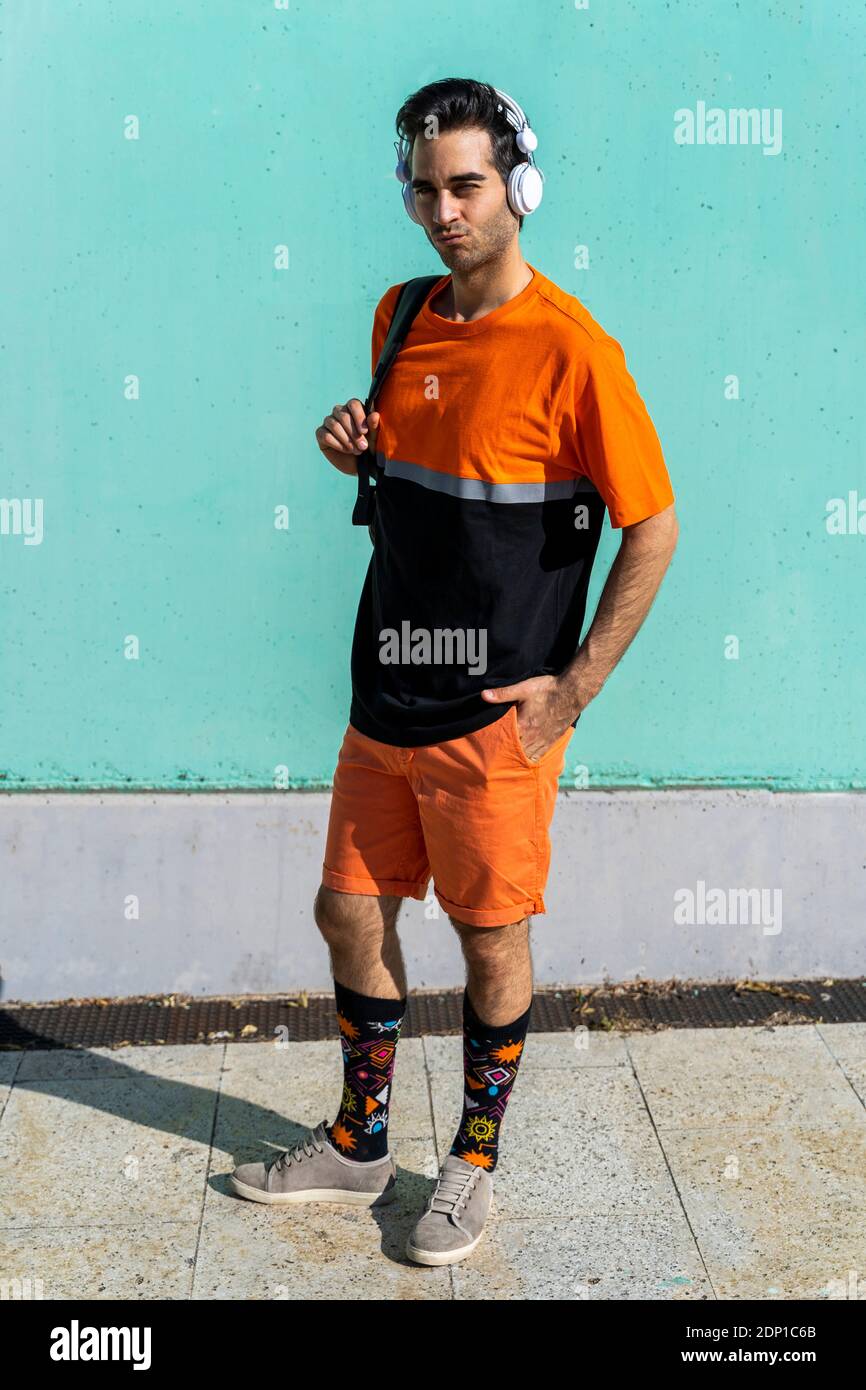 Cool homme debout devant le mur vert, en écoutant de la musique avec des écouteurs Banque D'Images