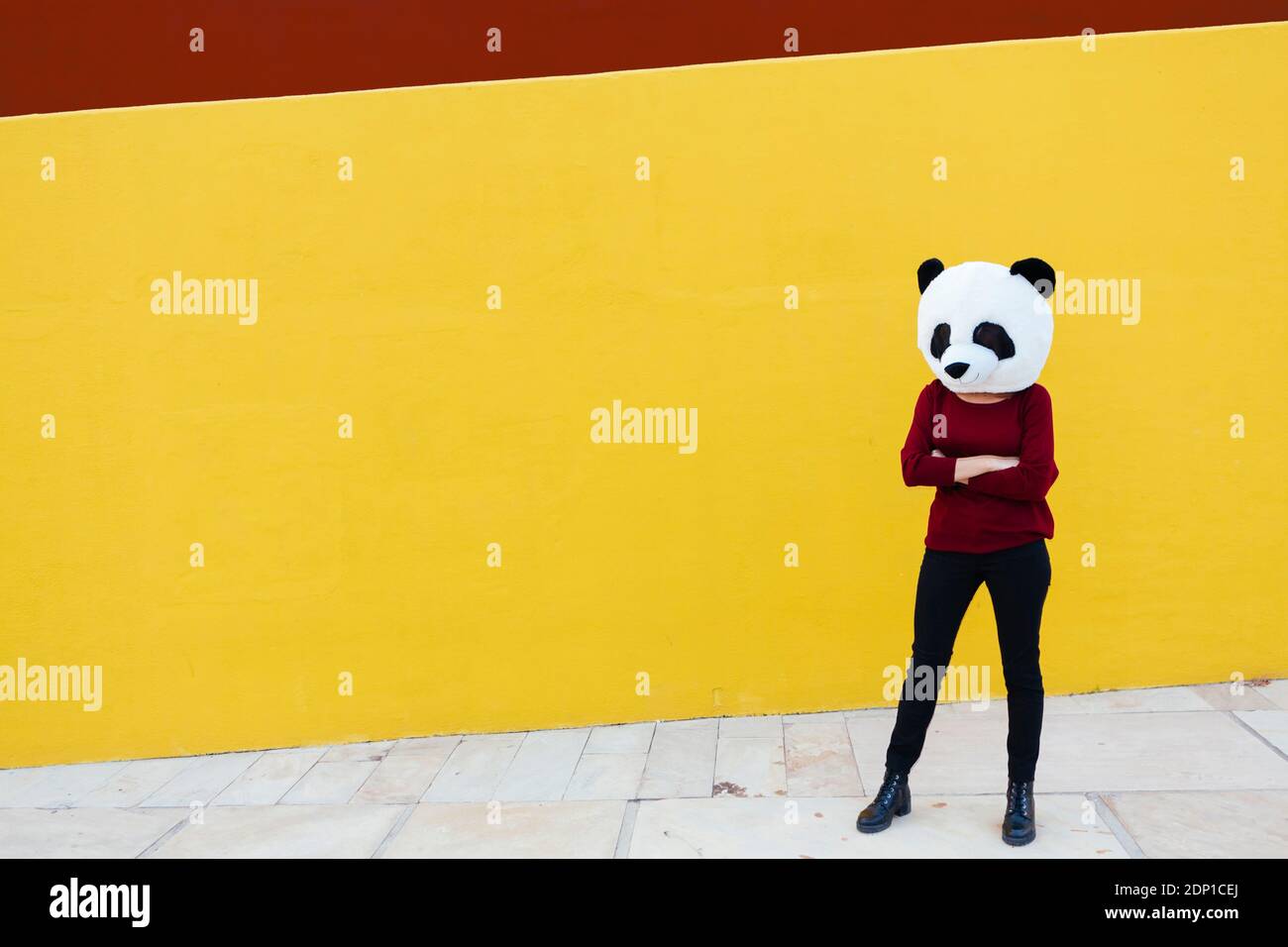 Femme aux bras croisés portant un masque de panda tout en se tenant contre mur jaune Banque D'Images