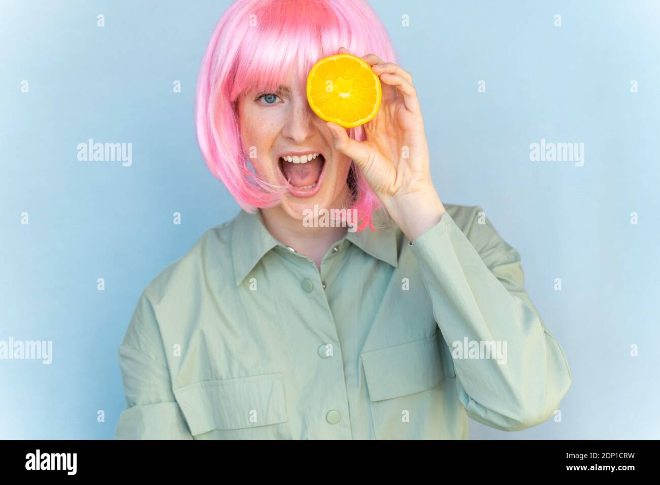 Portrait d'une jeune femme insouciante portant une perruque rose tenant un orange Banque D'Images