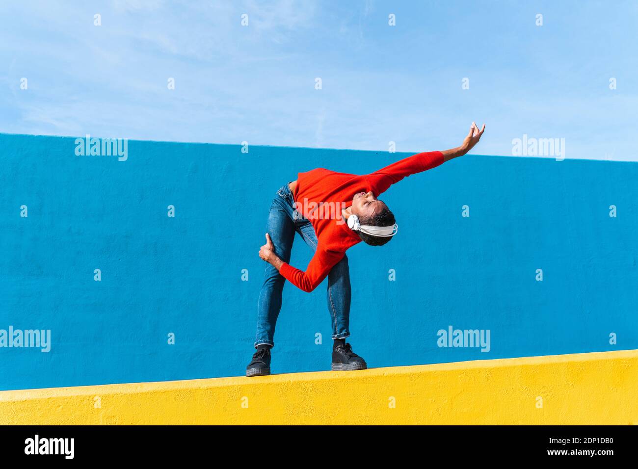 Jeune homme avec des écouteurs, l'écoute de la musique, de la danse sur le mur jaune Banque D'Images