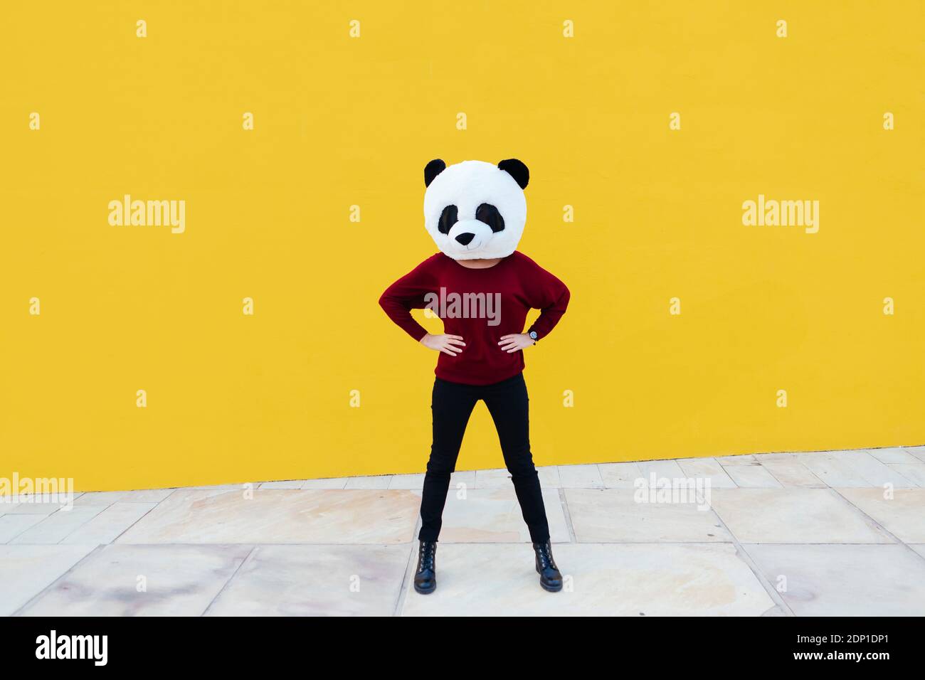 Femme à la main sur la hanche portant un masque de panda debout contre le mur jaune Banque D'Images
