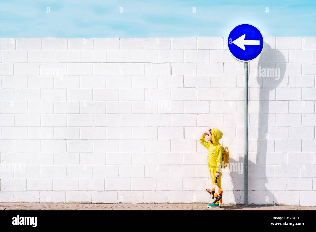 Fille avec son jouet mignon au panneau de signalisation, direction à gauche, devant un mur blanc Banque D'Images