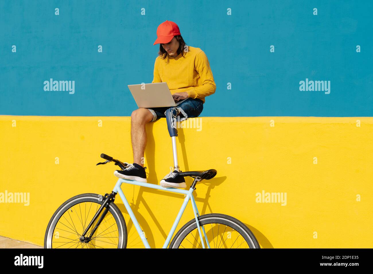 Homme avec un membre et un pied artificiels travaillant sur un ordinateur portable pendant assis sur un mur multicolore Banque D'Images