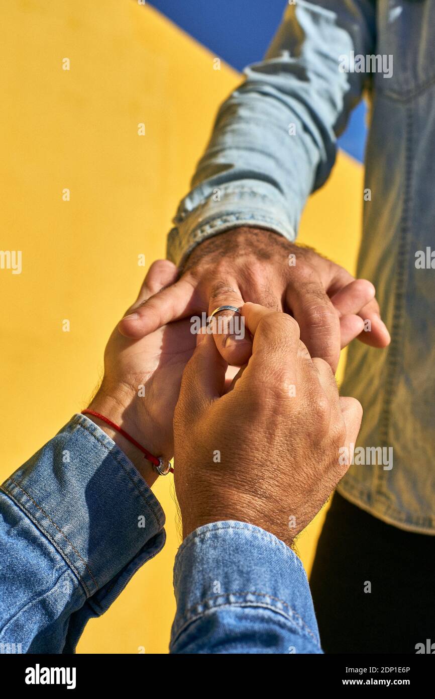 Gay homme mettant l'anneau dans le doigt jeune homme tout en se tenant par le mur jaune Banque D'Images