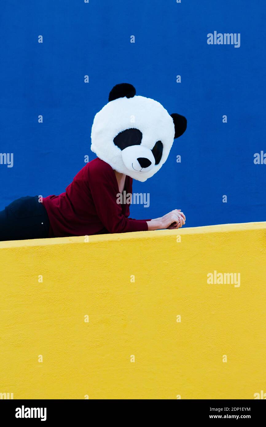 Femme portant un masque de panda tout en étant couché contre le mur bleu Banque D'Images
