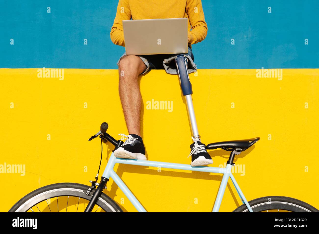 Homme avec un membre et un pied artificiels utilisant un ordinateur portable pendant qu'il est assis sur un mur multicolore Banque D'Images