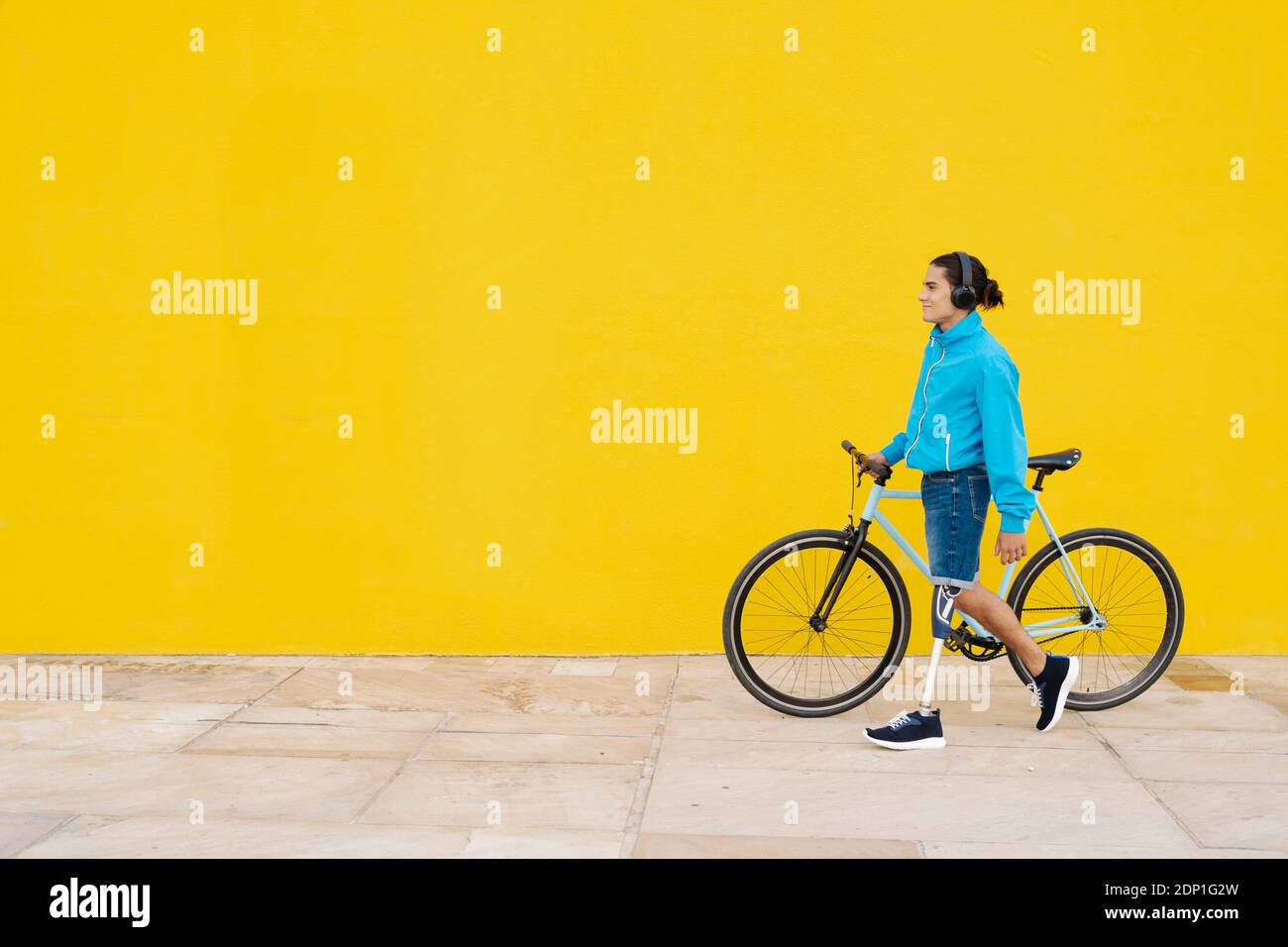 Homme avec un membre artificiel et un pied marchant avec un vélo contre mur jaune Banque D'Images