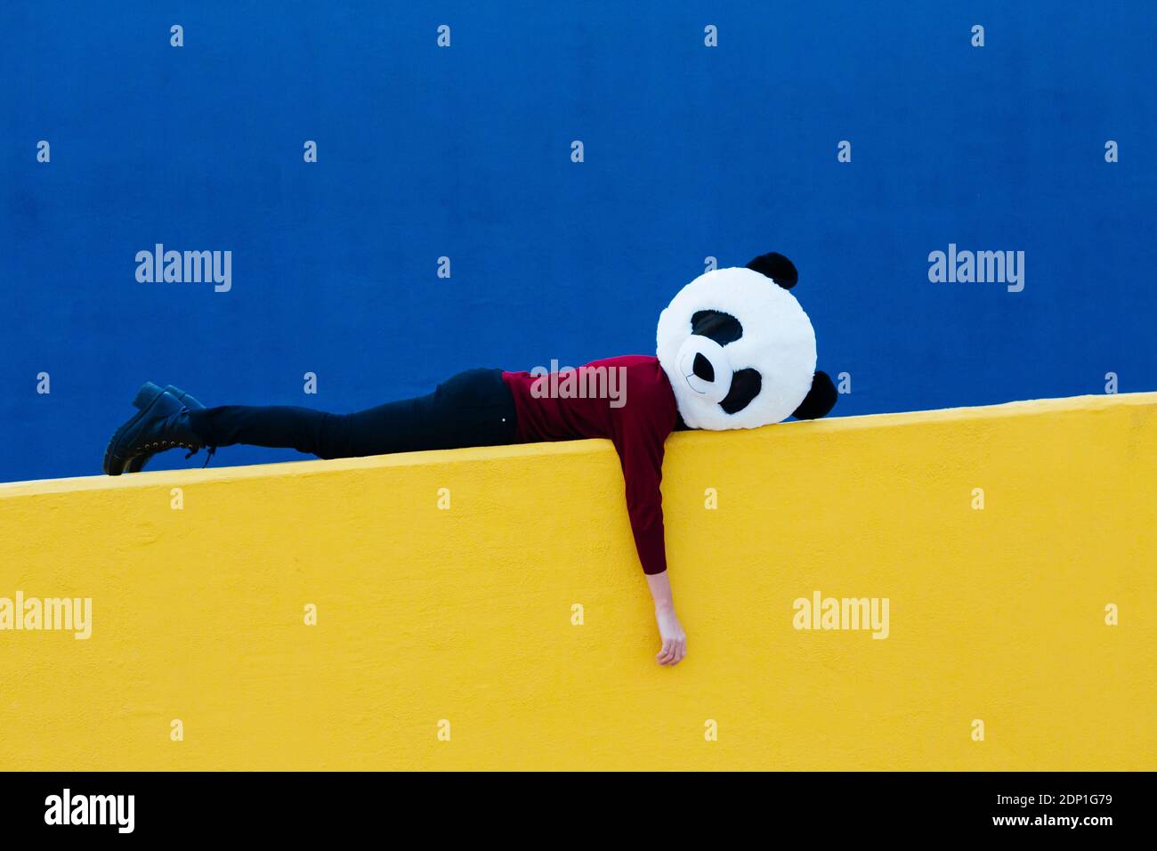 Femme portant un masque de panda sur un mur de soutènement jaune Banque D'Images