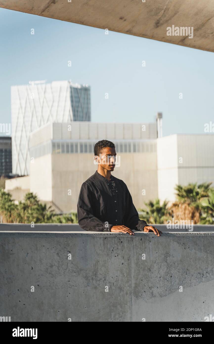 Jeune homme portant un caftan noir derrière un mur en béton Banque D'Images