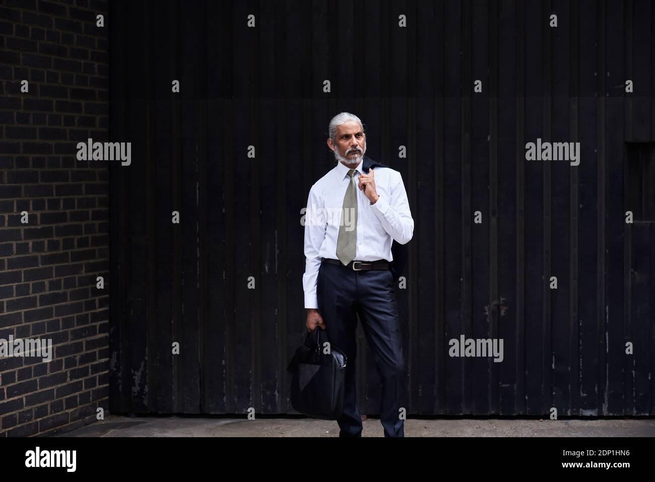 Portrait de senior businessman élégant avec des cheveux gris debout sur un fond sombre Banque D'Images