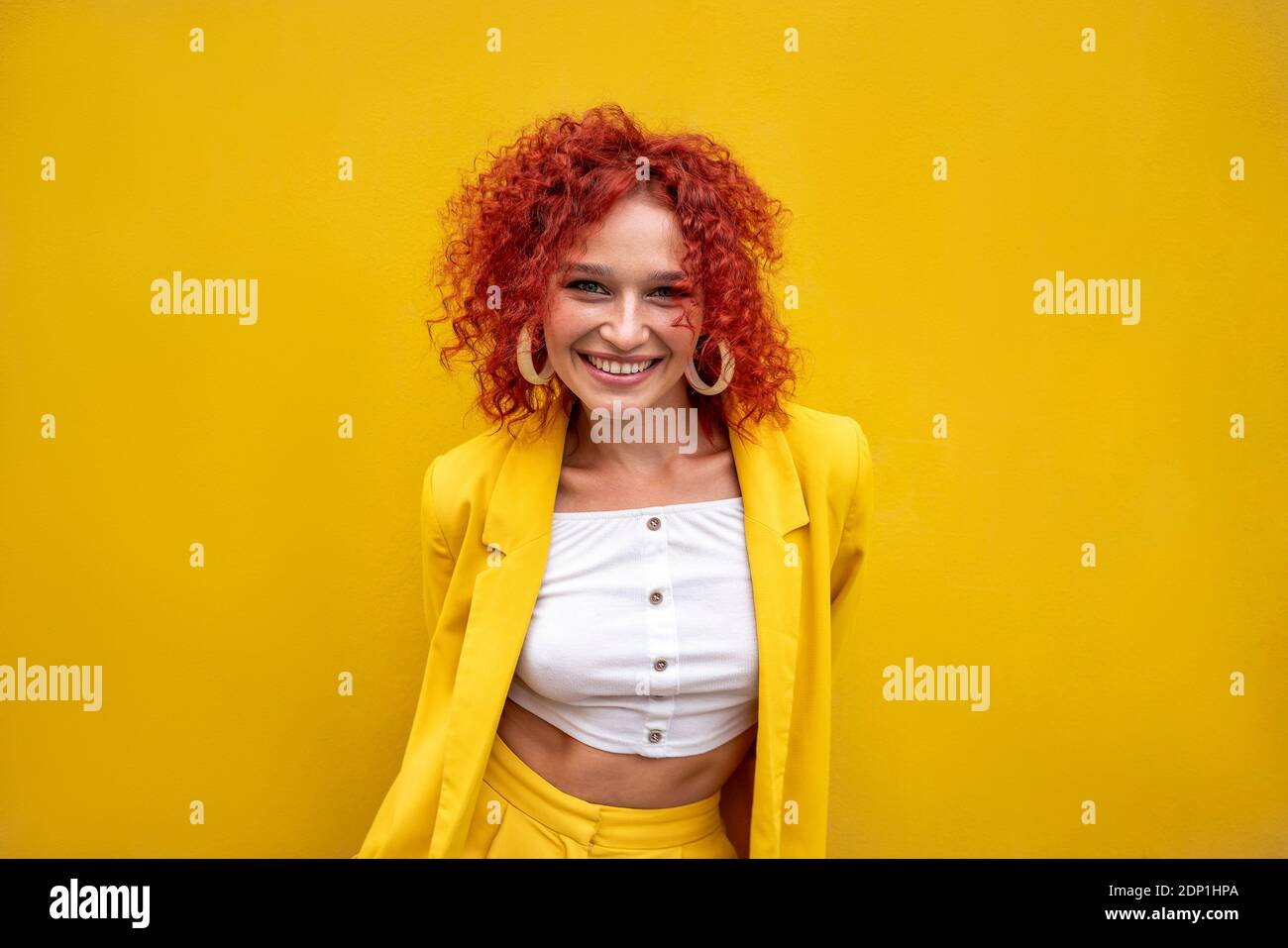 Bonne jeune femme avec des cheveux bouclés rouges devant mur jaune Banque D'Images Bonne jeune femme avec des cheveux bouclés rouges devant mur jaune Banque D'Images