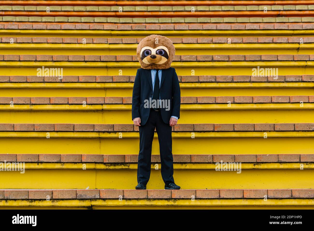 Homme d'affaires en costume noir avec masque de meerkat debout sur les escaliers Banque D'Images